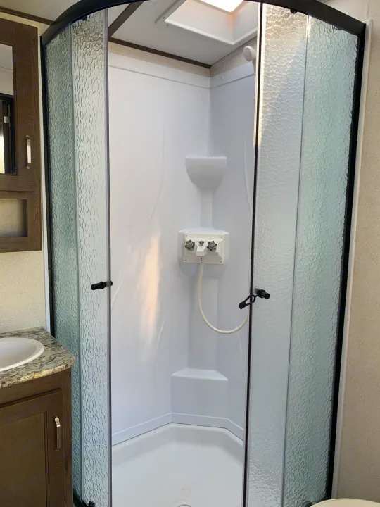 Modern corner RV rental shower featuring textured glass doors, white interior, and skylight for a bright experience.. Keystone Passport 2020
