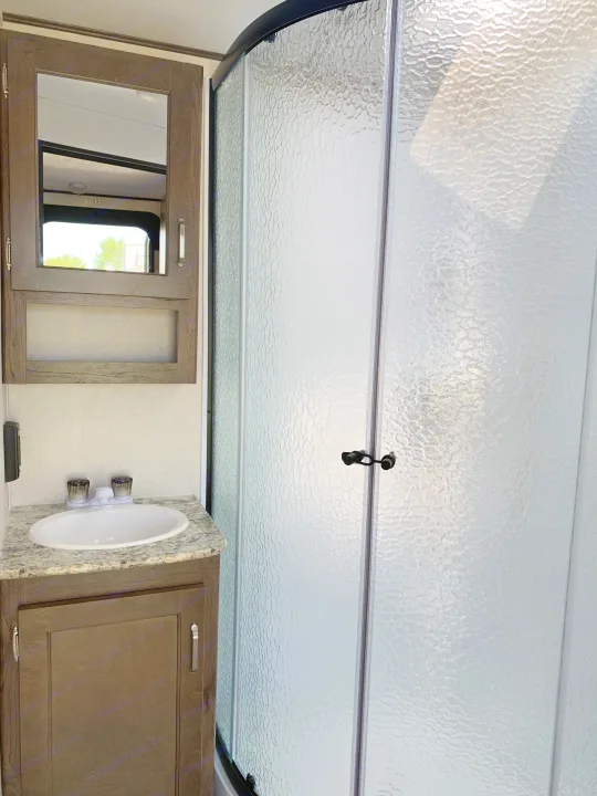 RV rental bathroom: Features a sink vanity, mirrored cabinet, and curved shower with textured glass doors.. Keystone Passport 2020