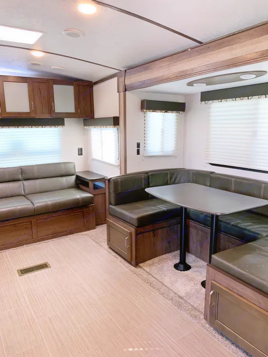 Spacious RV rental interior featuring a comfy sofa, U-shaped dinette, and overhead cabinets for a cozy travel living space.. Keystone Passport 2020