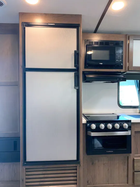 Inside an RV rental, a compact kitchen features a Dometic refrigerator, microwave, and a Furrion stove with oven.. Keystone Passport 2020