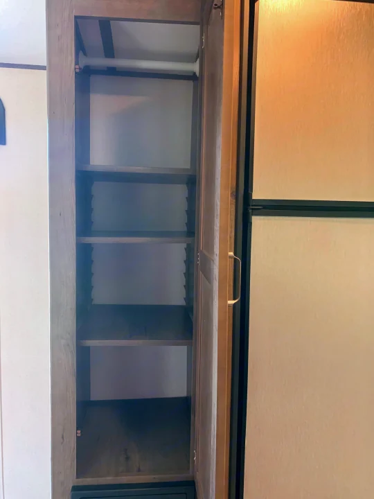 Spacious RV rental closet and pantry with a hanging rod and multiple shelves, next to a refrigerator. Great storage.. Keystone Passport 2020