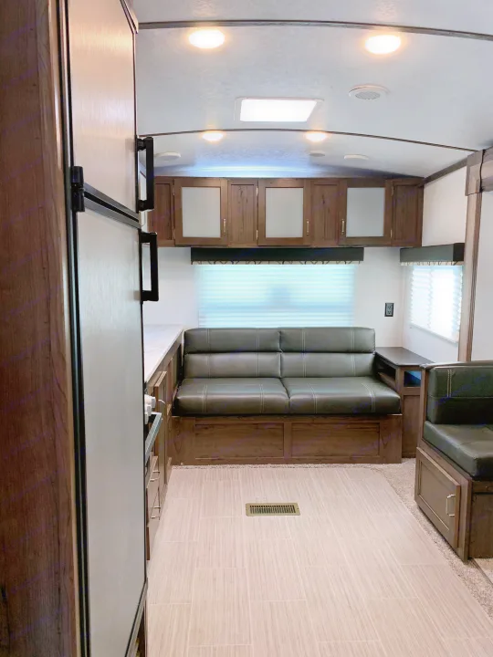 Bright RV rental interior with a dark sofa, light wood-look flooring, overhead cabinets, and skylight. Ready for adventure.. Keystone Passport 2020