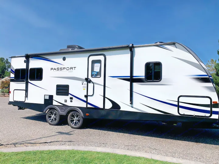 White Passport travel trailer with blue and black graphics, parked on gravel. This unit is sold; explore RV rental options!. Keystone Passport 2020