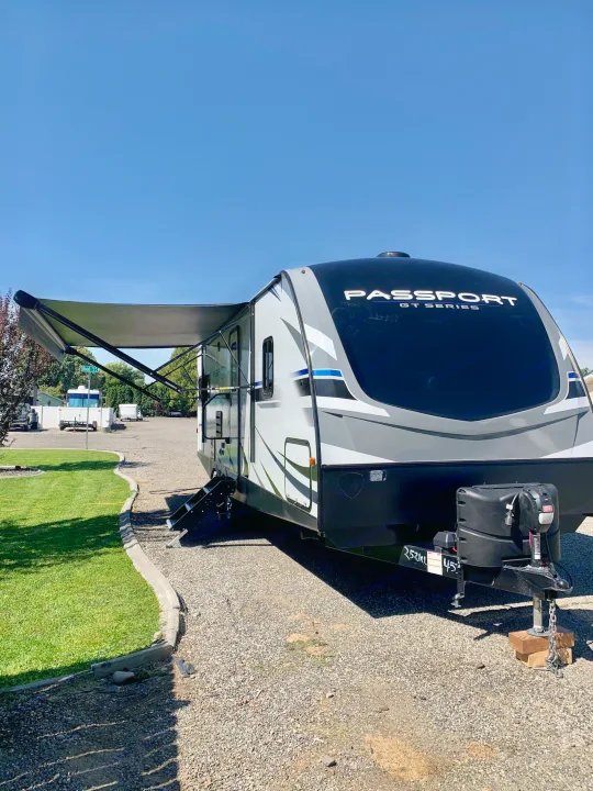 A sleek white & black Passport GT Series travel trailer, with its awning open, ready for your RV rental adventure on a sunny day.. Keystone Passport 2020
