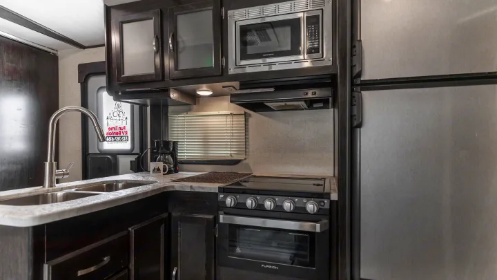A well-equipped RV rental kitchen featuring a sink, microwave, range, oven, and refrigerator, ready for travel cooking.. Coachmen Spirit Of America 2019