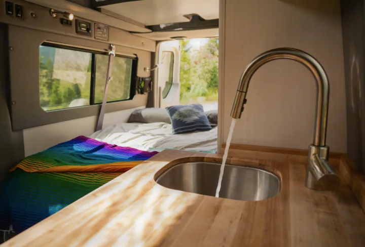 Inside this RV rental: a compact kitchen with running water, and a comfortable bed for road trip comfort. Van life ready!. Mercedes-Benz Sprinter 2020