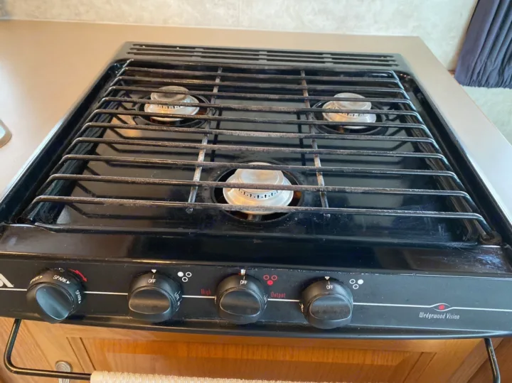 This image shows a black three-burner gas cooktop, common in an RV rental, with control knobs for cooking.. Ford Cutaway 2006