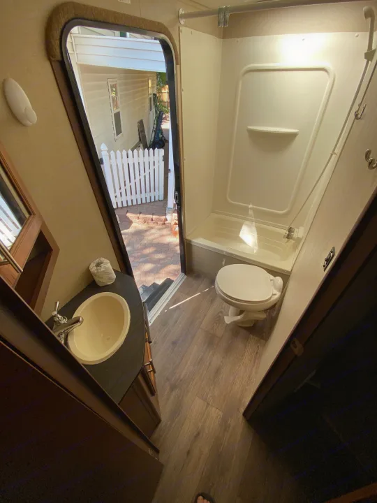 An RV rental bathroom interior: sink on left, toilet & shower on right. Open door reveals outdoor patio. Perfect for travel!. Dutchmen Aerolite 2015