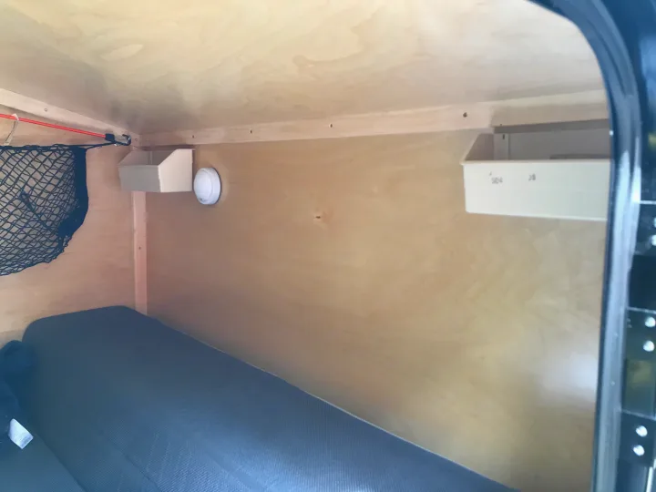 Cozy RV rental interior showing a small bed, wooden walls, overhead storage net & bins, and a safety detector.. Other Other 2020
