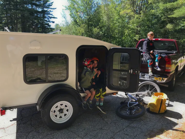Kids relaxing at their rv rental campsite, ready for adventure with bikes & gear, next to a red pickup truck.. Other Other 2020
