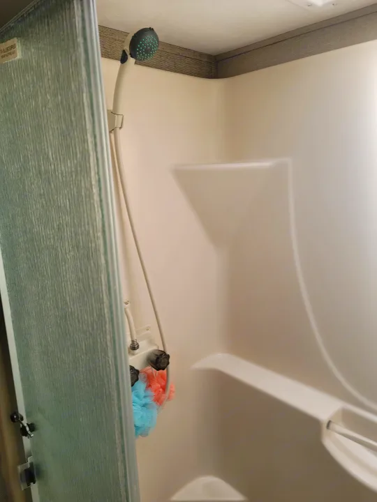 Compact RV rental shower interior with white walls, shower head, bath poufs, and frosted door panel.. Keystone RV Cougar 2018