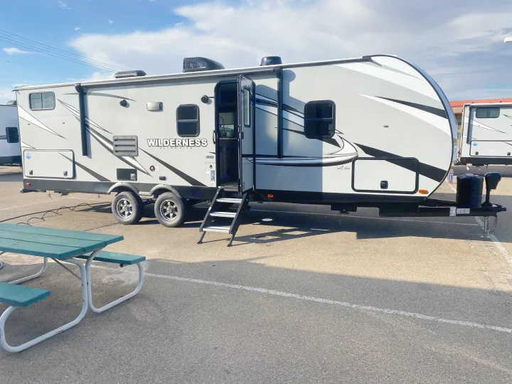 RV rental: Grey Wilderness travel trailer with open door & steps, parked on asphalt near a green picnic table.. Heartland Wilderness 2021