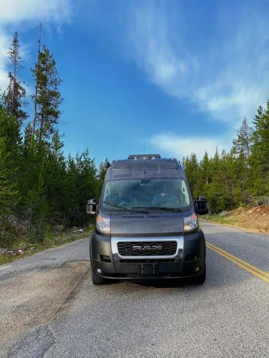 Explore nature with this RV rental camper van on a scenic forest road. Two people enjoy the journey.. Thor Tellaro 2020