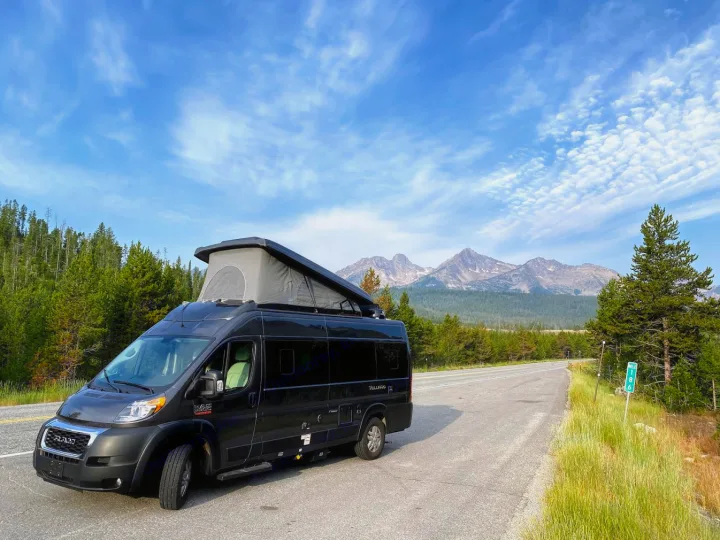 Black RV rental van with pop-top extended, parked roadside. Majestic mountains and forests define this scenic travel.. Thor Tellaro 2020