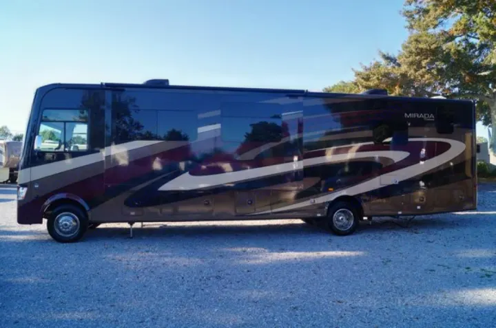 A large, dark Mirada RV with tan and maroon stripes is parked on gravel, an excellent option for your next RV rental.. Coachmen Mirada 2016