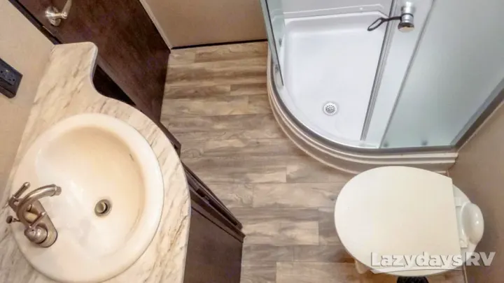 RV rental bathroom features: marble-top sink, curved shower, and toilet on wood-look flooring.. Coachmen Chaparral 2018