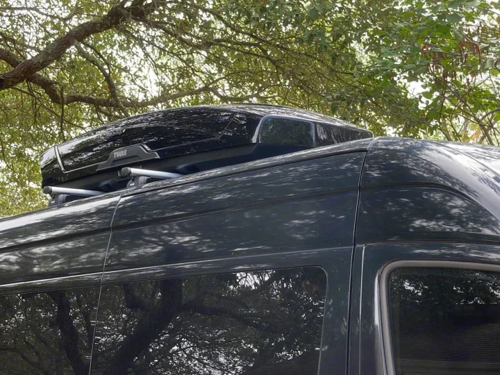 Dark-colored **rv rental** van with a Thule roof cargo box and roof racks. Ideal for travel and gear storage.. Mercedes-Benz Sprinter 2015