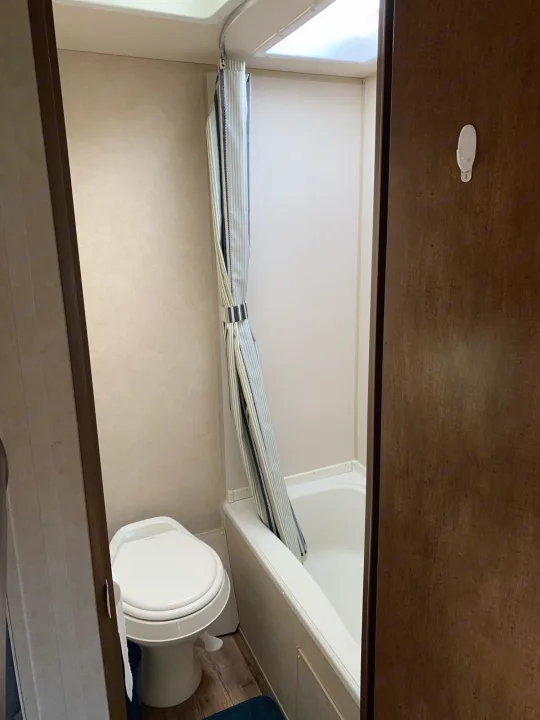 Inside an rv rental: a practical bathroom featuring a toilet, bathtub, and striped shower curtain.. Forest River Wildwood 2017