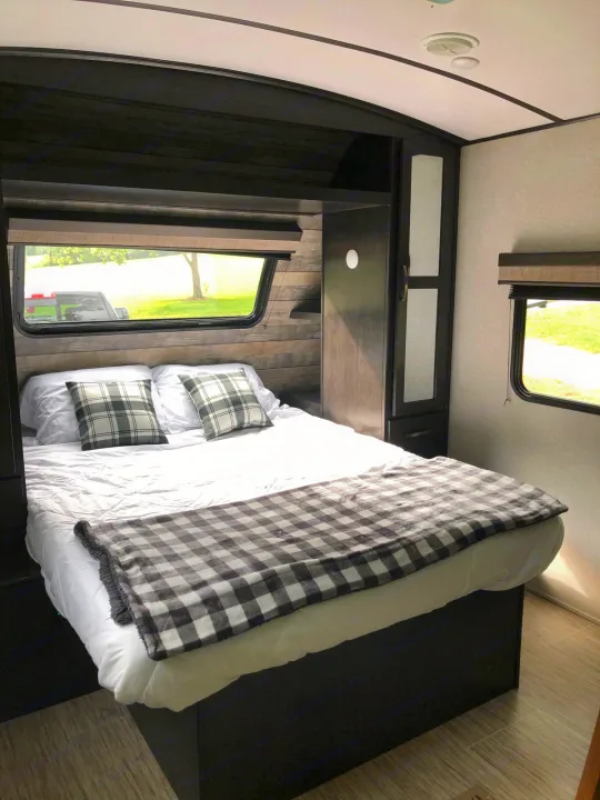 Comfortable RV rental bedroom with modern decor, featuring a neatly made bed with plaid pillows, built-in cabinets, and large windows.. ForestRiver Surveyor 2020