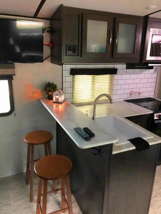 Step inside this cozy RV rental! Features a modern kitchen with a breakfast bar, TV, and subway tile backsplash. Ideal for travel.. ForestRiver Surveyor 2020