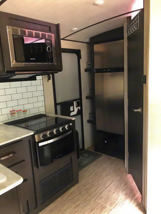 Modern RV rental kitchen featuring a microwave, stove, fridge, and stylish dark cabinets with white backsplash.. ForestRiver Surveyor 2020