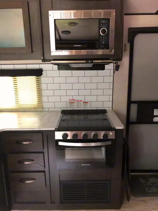 This RV rental kitchen features modern appliances like a microwave, stovetop, and oven, with subway tile backsplash.. ForestRiver Surveyor 2020