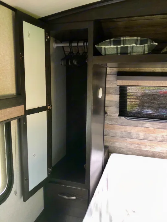 Cozy RV rental bedroom with open closet, hangers, drawer, bed, and plaid pillow on shelf.. ForestRiver Surveyor 2020