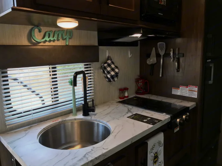 Clean RV rental kitchen with white marble counters, sink, stovetop, microwave, and rustic camp decor.. Forest River Wolf Pup 2021