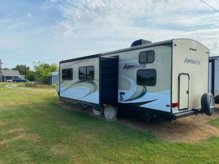 This spacious beige Aerolite travel trailer, potentially an RV rental, is parked on a grassy lot with its slide-out extended.. Dutchmen Aerolite 2017