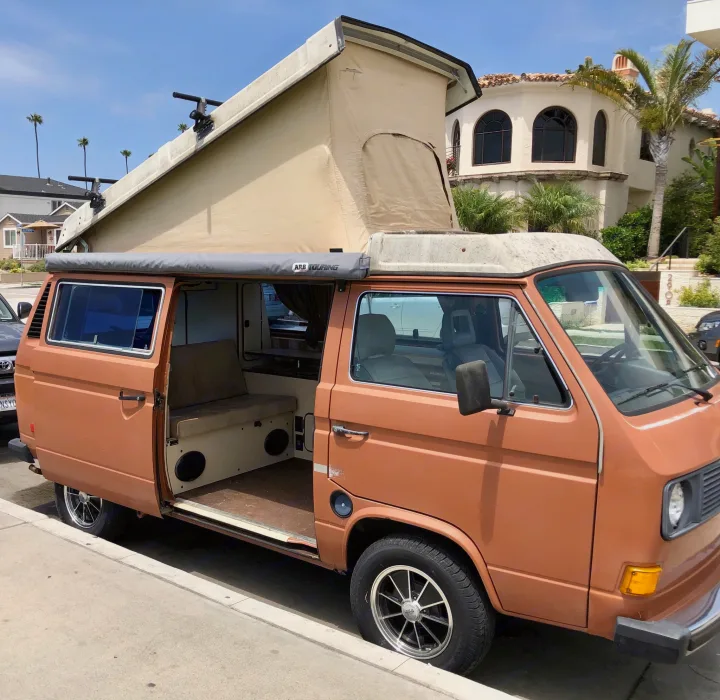 A classic orange VW Vanagon pop-top camper van with an ARB awning, ready for an RV rental adventure.. Volkswagen Westfalia 1982