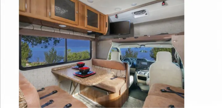 Spacious RV rental interior featuring a comfortable dinette with a beautiful lake view through a large window. Ideal for road trips.. Thor 28A 2019