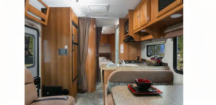 RV rental interior: practical living space with a kitchen, dining area, and rear bedroom. Wood finishes and functional design.. Thor 28A 2019