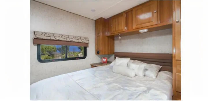 Comfortable RV rental bedroom with a large bed, overhead cabinets, and a scenic window view.. Thor 28A 2019