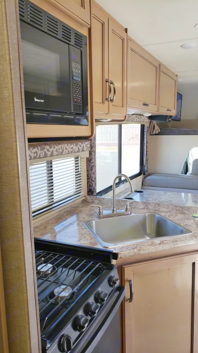 Spacious RV rental kitchen: microwave, stove, sink, light wood cabinets, dinette, and TV.. Thor 28A 2019