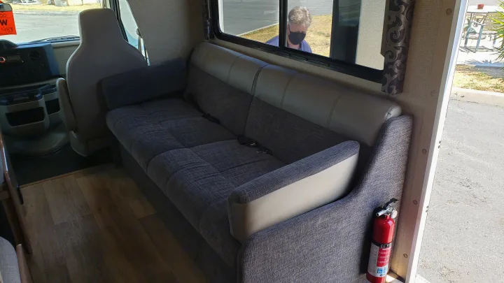 Spacious RV rental interior showcasing a comfortable sofa, wood flooring, and a mounted fire extinguisher for safety.. Thor 28A 2019