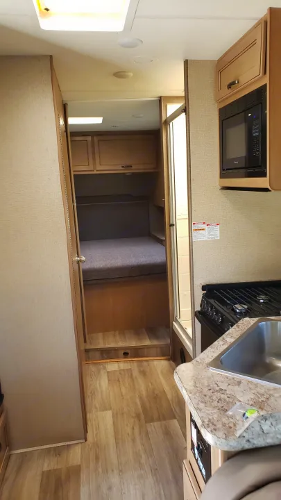 RV rental interior shows a compact kitchen with stove, microwave, sink, and a hallway leading to bunk beds and a bathroom.. Thor 28A 2019