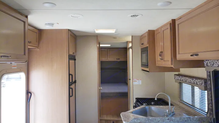 Interior of an RV rental: kitchen with sink and stove, refrigerator, living space, and bunk beds in the rear.. Thor 28A 2019