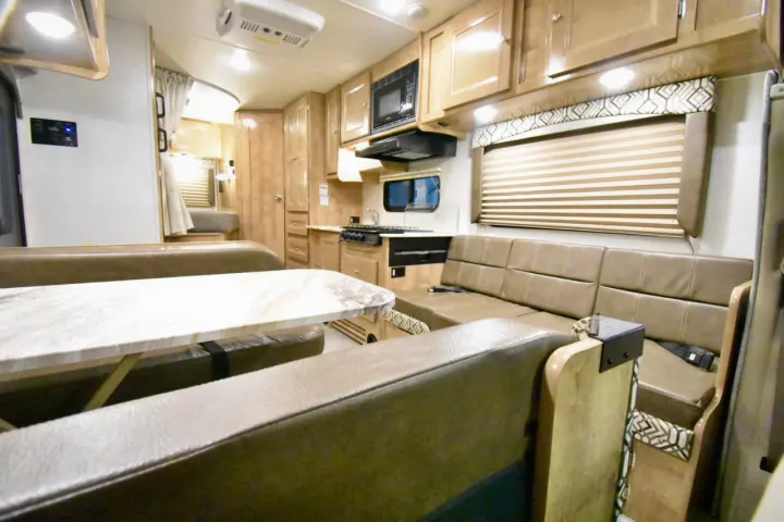 Cozy RV rental interior showcasing a brown dining booth, matching sofa, and a fully-equipped kitchen with cabinetry.. Leprechaun 230RB 2020
