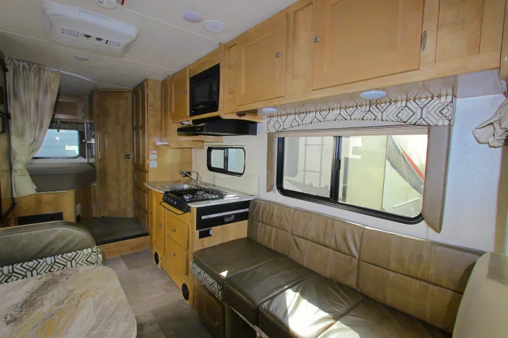Inside this RV rental, find a compact kitchen with stove, microwave, sink, and light wood cabinets, plus a comfy dinette.. Leprechaun 230RB 2020