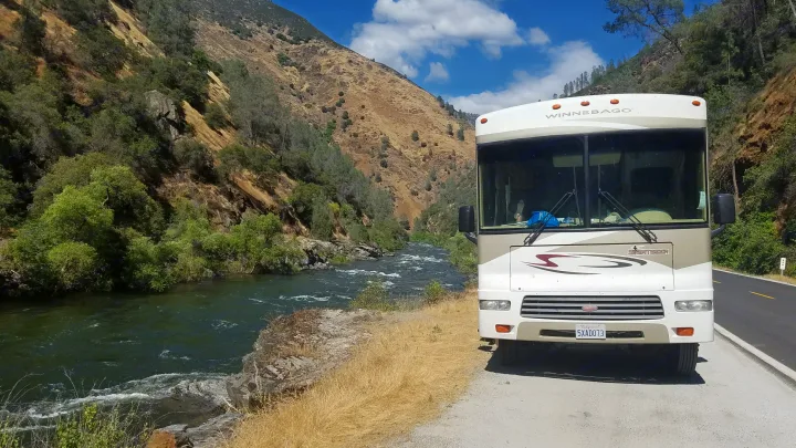 RV rental parked by a swift river in a mountain canyon. A Winnebago Sightseer, with feet relaxing inside.. Winnebago Sightseer 2007