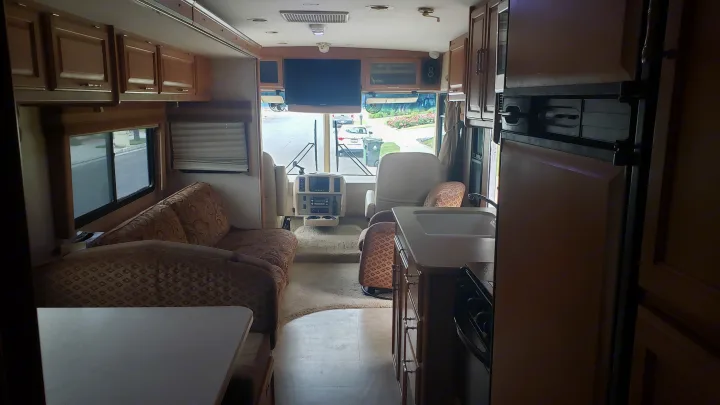 Experience this rv rental interior: view of the kitchen, living area with a couch, and the front driver's cockpit.. Winnebago Sightseer 2007