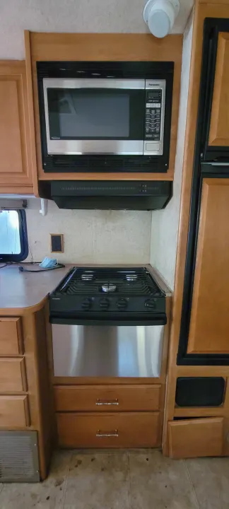 Compact RV rental kitchen showcasing a microwave, Dometic stove, oven, refrigerator, and wood cabinetry.. Winnebago Sightseer 2007