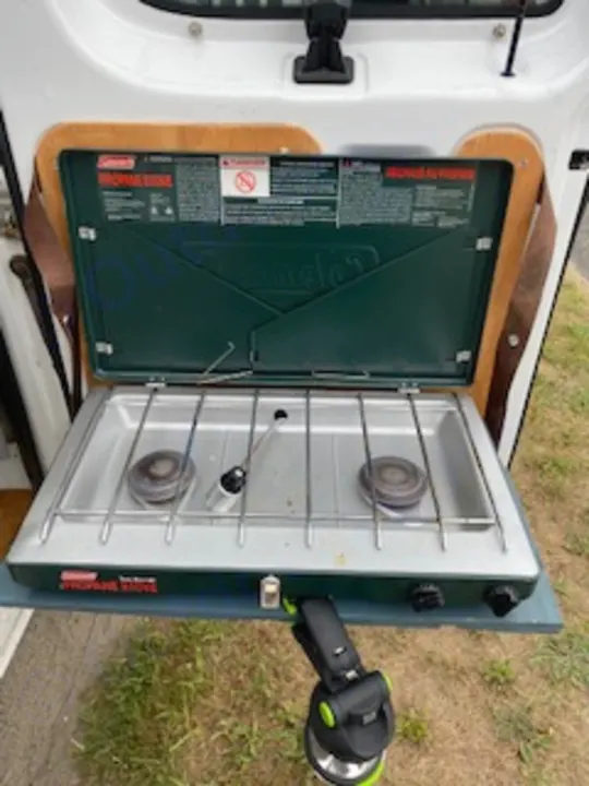 Coleman 2-burner camping stove, part of an RV rental's outdoor kitchen setup for campsite cooking.. Ford Econoline E250supercab 1999