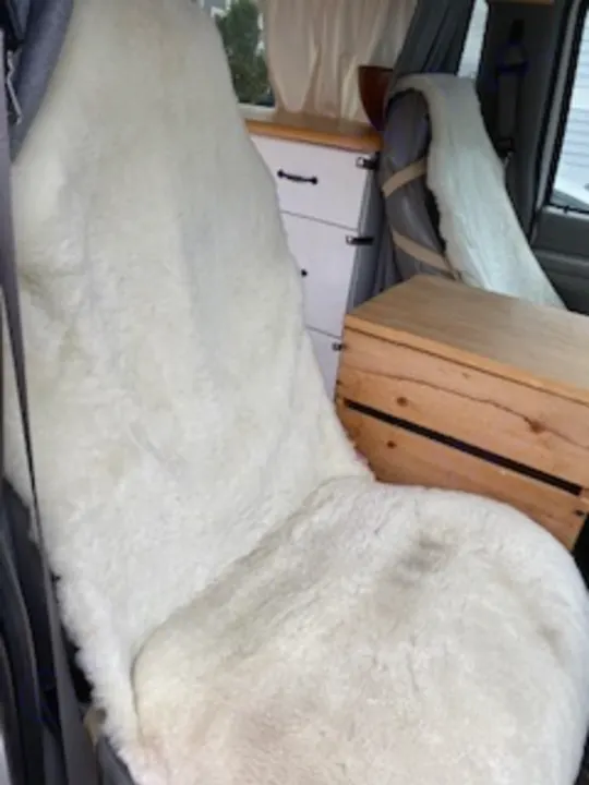 Cozy RV rental interior: plush white sheepskin on a campervan bed/seat, with practical wood crate and cabinets.. Ford Econoline E250supercab 1999