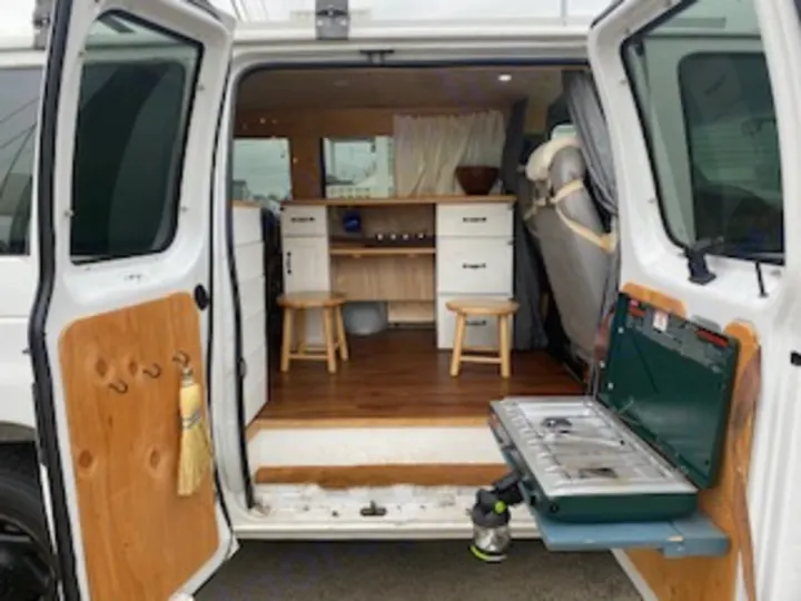 This RV rental offers a glimpse inside a custom camper van with a cozy kitchen and outdoor cooking setup.. Ford Econoline E250supercab 1999
