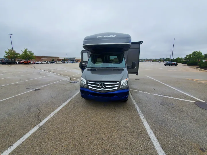 Front view of a grey Mercedes-Benz Pulse RV rental with blue trim, parked in a wet lot. Driver's door is open.. Fleetwood Pulse 2019