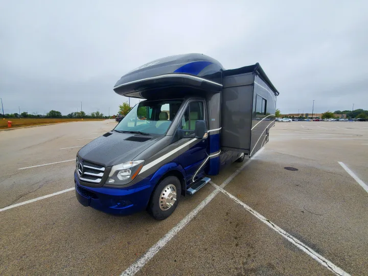 A blue and grey Mercedes-Benz Sprinter RV rental is parked in a wet lot under overcast skies. An ideal camper for travel.. Fleetwood Pulse 2019