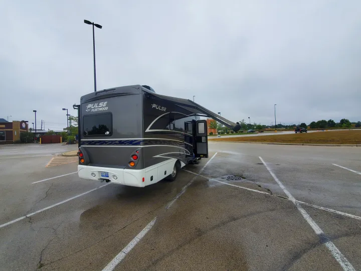 Gray and white Fleetwood Pulse RV rental motorhome with extended awning, parked in a wet lot.. Fleetwood Pulse 2019