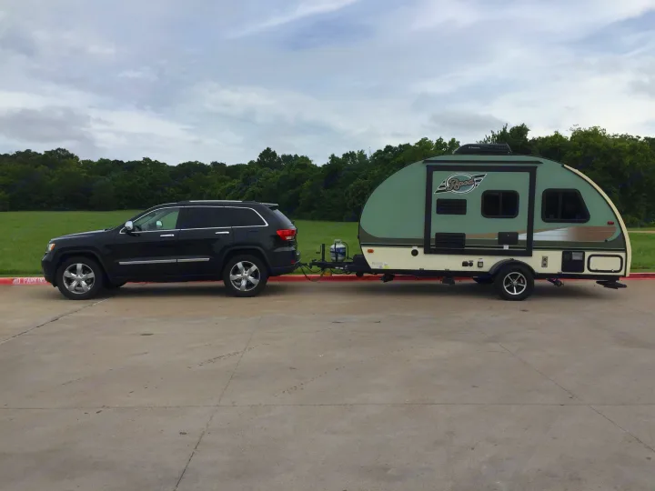 Black SUV towing a green and cream teardrop RV, ideal for an rv rental adventure. Parked on concrete with green background.. Other Other 2016
