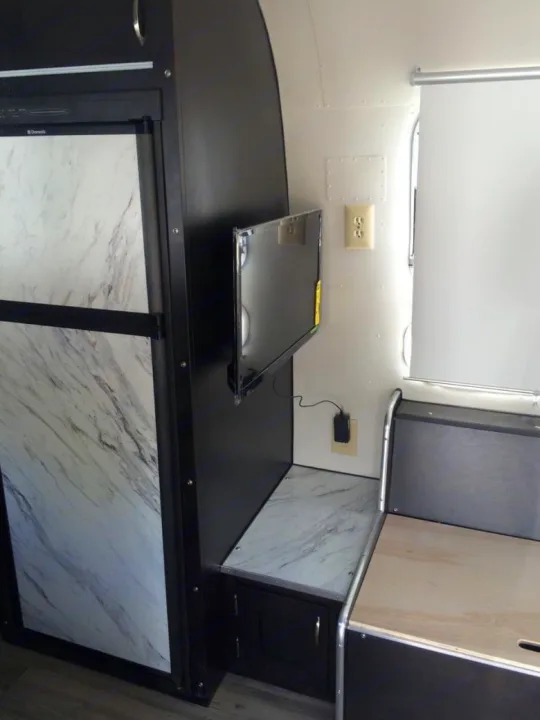 Modern RV rental interior with a Dometic fridge, wall-mounted TV, and light wood dinette seating.. Airstream Sovereign 1973